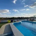 The sun deck of a Nile Cruise ship with a rectangular swimming pool, bordered by a synthetic green lawn and bright yellow and blue beanbag chairs, under a clear blue sky.