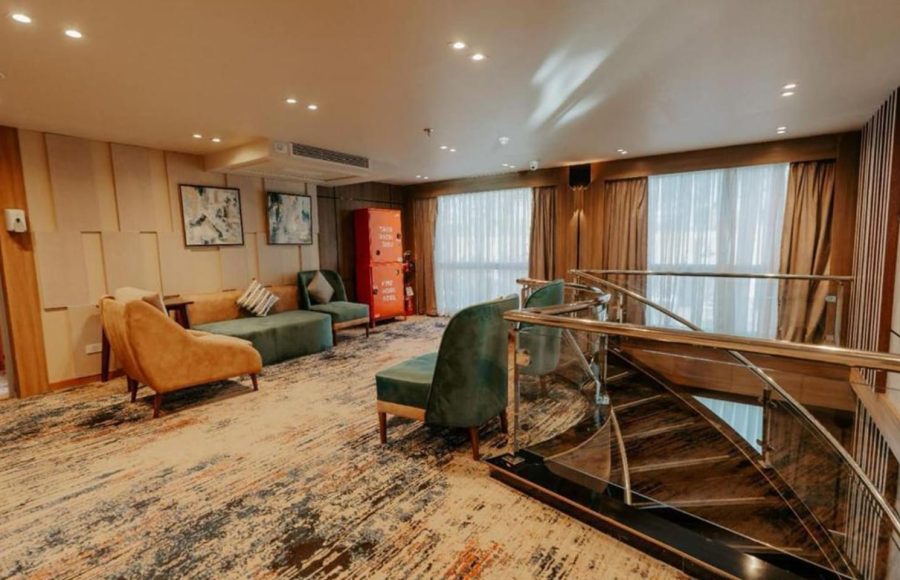 A contemporary lounge area on a Nile Cruise ship with a spiral staircase, featuring a patterned carpet, modern furniture in gold and deep green velvet, and large windows with heavy drapes.