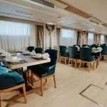 The elegant dining area of a Nile Cruise ship, featuring multiple wooden tables set with white china and paired with deep teal or royal blue velvet upholstered dining chairs.