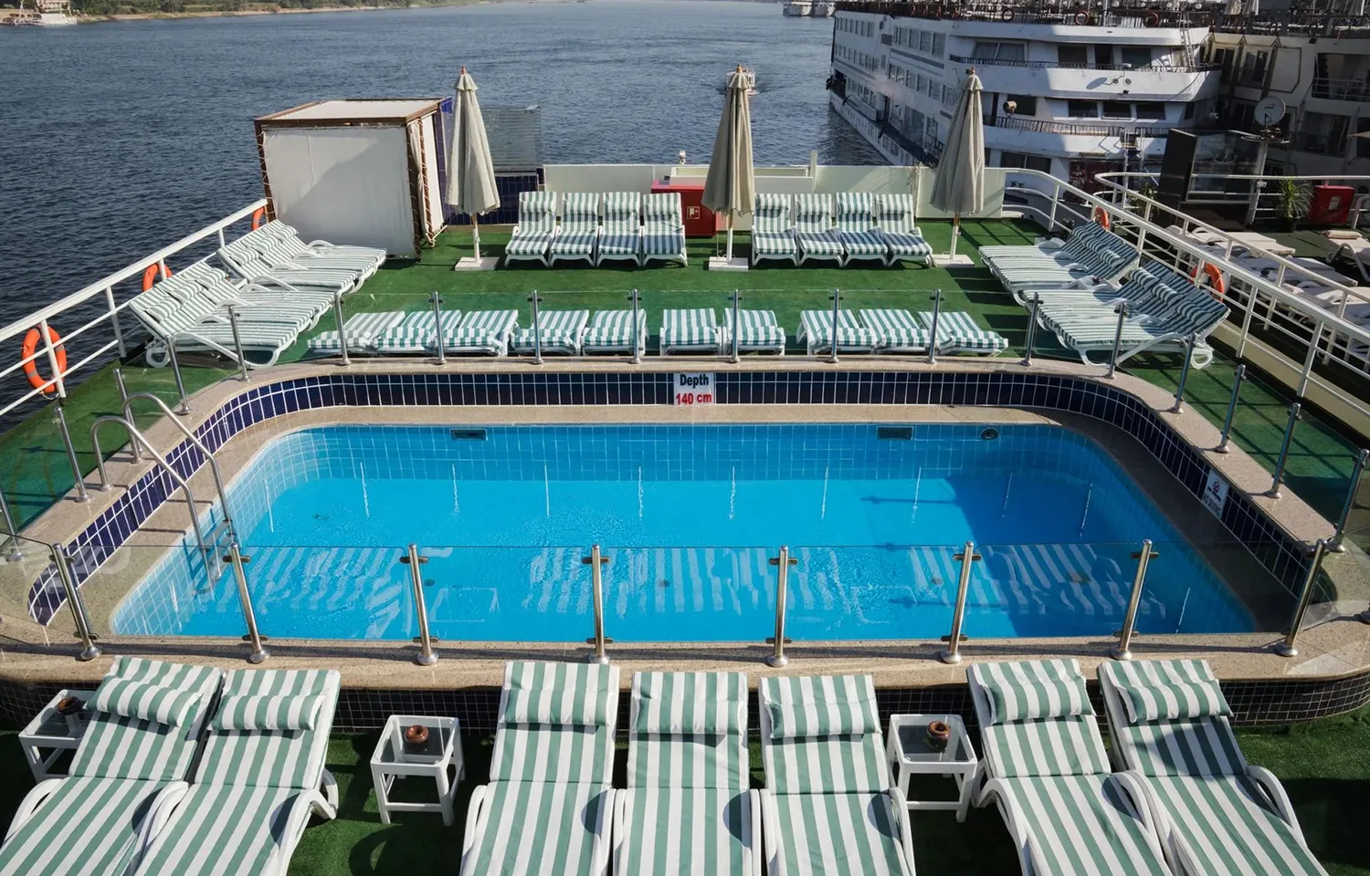 Sun deck with a rectangular swimming pool and striped lounge chairs on the Commodore Nile Cruise boat.