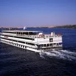 A large white and red Cruising ship on the Nile river Egypt sailing past palm-lined banks, symbolizing a fantastic part of a cairo nile cruise hurghada adventure.