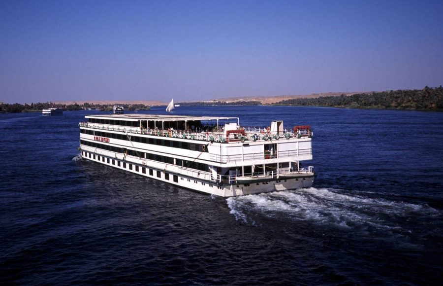 A large white and red Cruising ship on the Nile river Egypt sailing past palm-lined banks, symbolizing a fantastic part of a cairo nile cruise hurghada adventure.