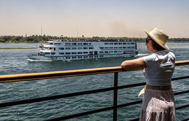 A woman in a sun hat watching another ship pass by during a dahabiya nile cruise tour 12 days.