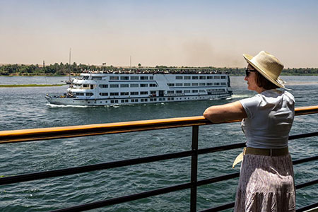 A woman in a sun hat watching another ship pass by during a dahabiya nile cruise tour 12 days.