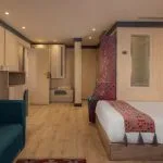 Interior of a spacious Nile cruise ship bedroom with a bed, a teal sofa, and patterned bedding, decorated with Egyptian motifs.