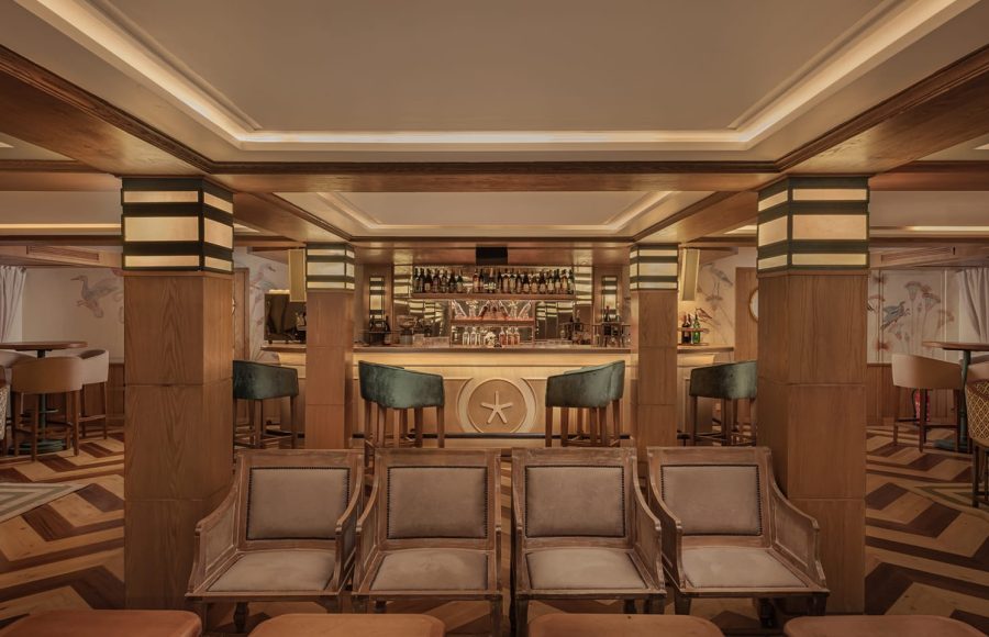 Interior of a sophisticated cruise ship lounge and bar with wood paneling, velvet barstools, and comfortable armchairs.