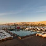 Swimming pool and rows of deck chairs on a cruise ship at sunset, overlooking the Nile River and desert mountains.