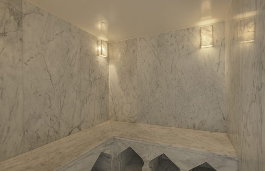 Interior of a luxury cruise ship spa steam room or hammam, featuring dark tiled walls, built-in benches, and soft colored lighting.