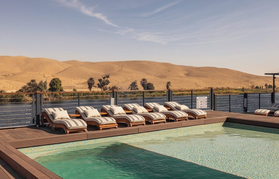 Swimming pool and deck chairs on a Nile cruise ship, with the desert hills and riverbank in the background.