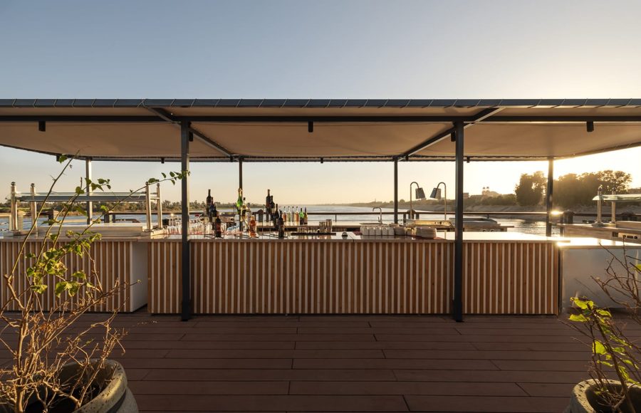 Outdoor bar on a cruise ship sundeck, featuring bottles of liquor and overlooking the water during golden hour.