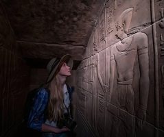 A tourist explores ancient carvings on Egypt tours from Australia. A tourist looking at ancient carvings inside an Egyptian tomb, a key experience on package tours to Egypt from Australia.