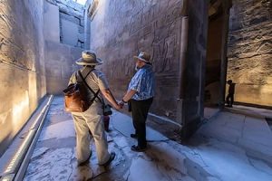 Tourists exploring hieroglyphics, a highlight of Egypt Tours From Canada. Tourists examining ancient hieroglyphics inside a temple, a key experience on Egypt holiday packages from Canada.