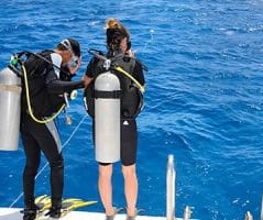 Scuba divers prepare to dive during Egypt travel from Bangladesh. Two scuba divers on a boat, getting ready to dive into the clear blue water during an Egypt trip from Dhaka.