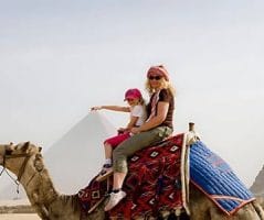 A Woman with her kid riding a camel, with the Great Pyramid of Giza prominently in the background, is a classic scene from Egypt archaeological trips and archaeological tours of Egypt.