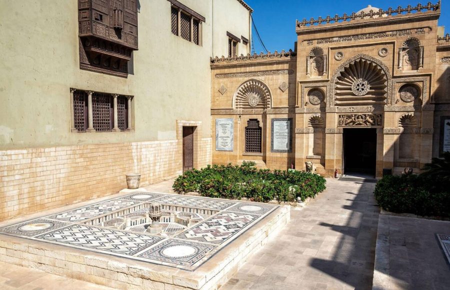 Exterior view of the Coptic Museum in Cairo Egypt, showing the museum's traditional courtyard architecture, a mosaic fountain, and a blend of stone and mashrabiya windows.