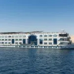 White, multi-deck Nile cruise ship with arched windows sailing in overcast conditions.