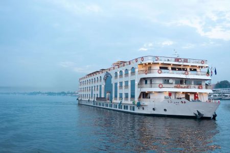 White, Multi-Deck Nile Cruise Ship With Arched Windows Sailing On The River At Dusk.