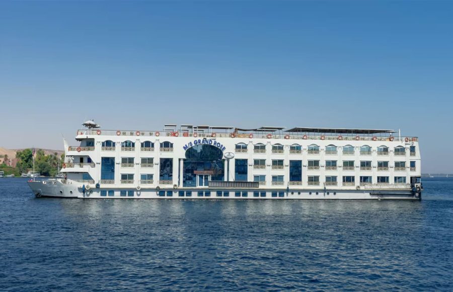 White, multi-deck Nile cruise ship with arched windows sailing in clear blue daylight.