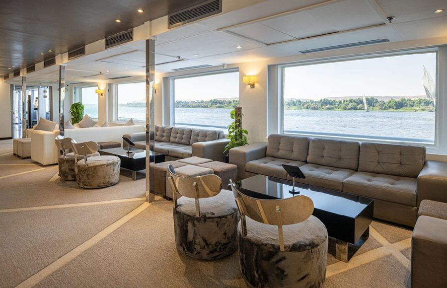 Spacious main lounge or bar area on the MS Farah cruise ship with large picture windows offering a panoramic view of the Nile.