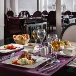 Elegantly set dining table in the MS Farah restaurant with four plated meals, wine, water glasses, and a bread basket.