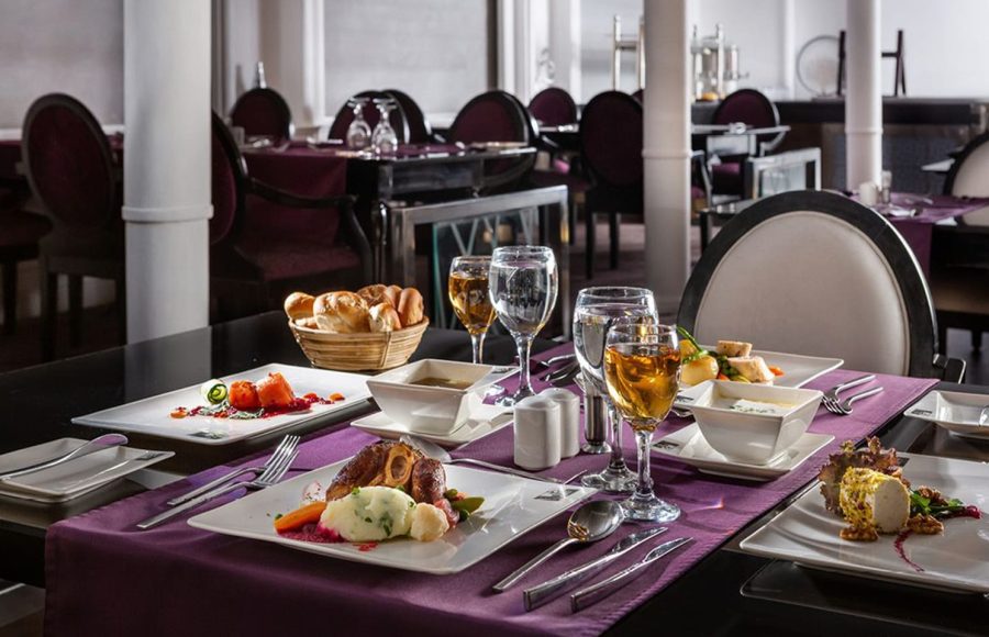 Elegantly set dining table in the MS Farah restaurant with four plated meals, wine, water glasses, and a bread basket.