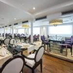 Elegantly set dining table in the MS Farah restaurant with four plated meals, wine, water glasses, and a bread basket.