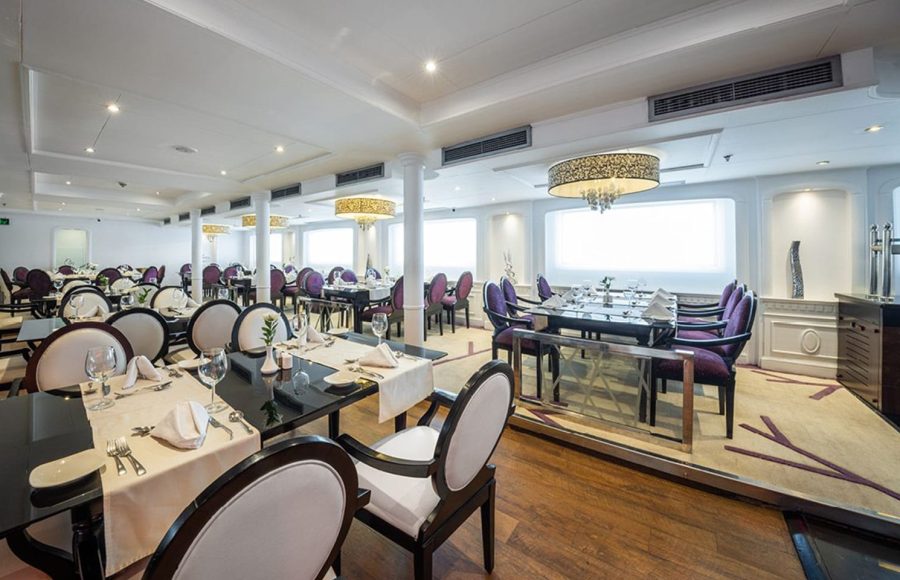 Elegantly set dining table in the MS Farah restaurant with four plated meals, wine, water glasses, and a bread basket.