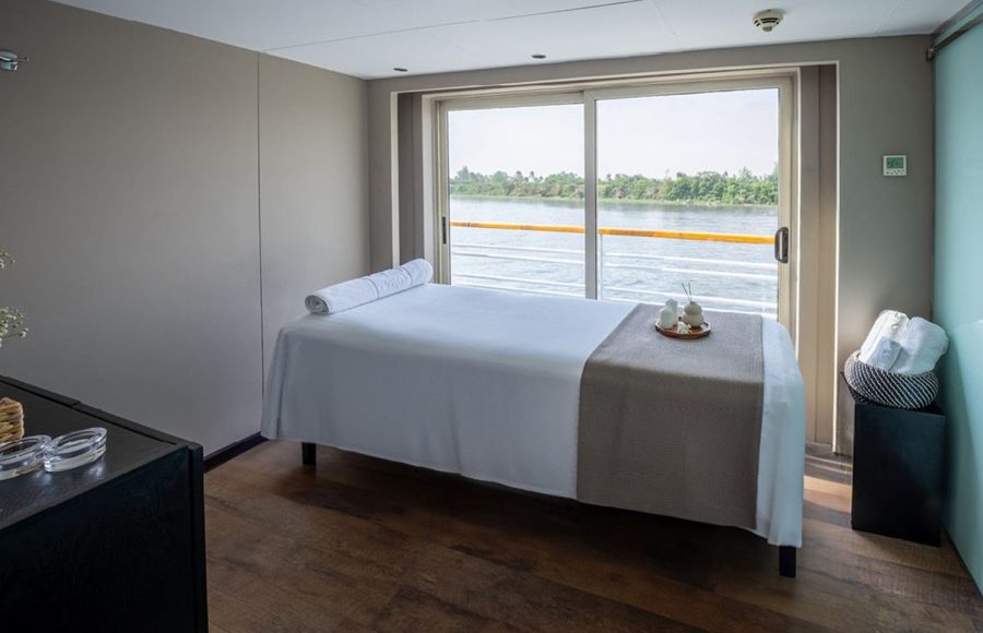 Massage treatment room on the MS Farah cruise ship with a massage bed and sliding glass door with a Nile view.