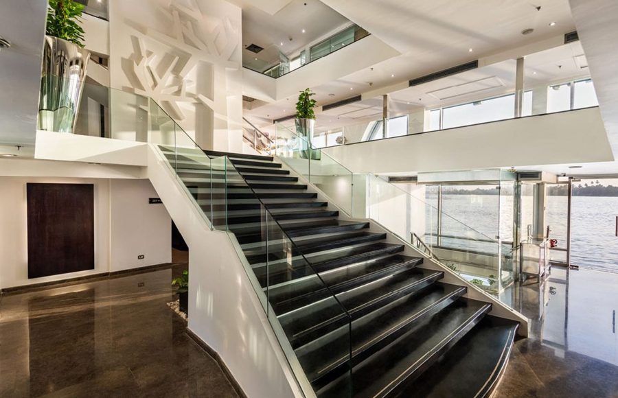 Grand central staircase in the MS Farah lobby, with black steps, white walls, and a glass railing, facing a view of the Nile.