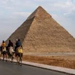 A group of tourists following a guide on a Giza camel tour past the Great Pyramid