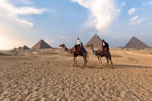 Great-Pyramids-of-Giza-couple-riding-camels-on-the-desert A tourist walks towards the grand entrance of the Temple of Edfu, a well-preserved ancient temple with carved stone facades.