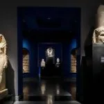 The dimly lit interior gallery of the Greco Roman Museum in Alexandria, Egypt, displaying ancient statues and artifacts under dramatic blue lighting.