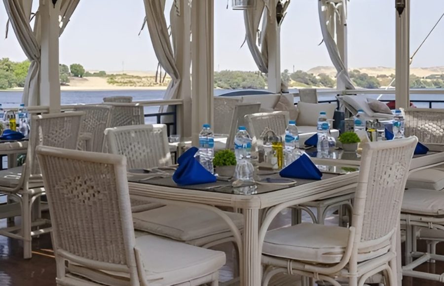 Outdoor dining tables with white chairs and blue napkins on a boat deck.
