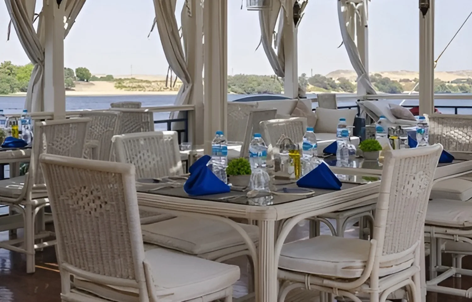 Outdoor dining tables with white chairs and blue napkins on a boat deck.