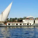 A white and gold Dahabiya sailing boat with two large sails on the Nile.