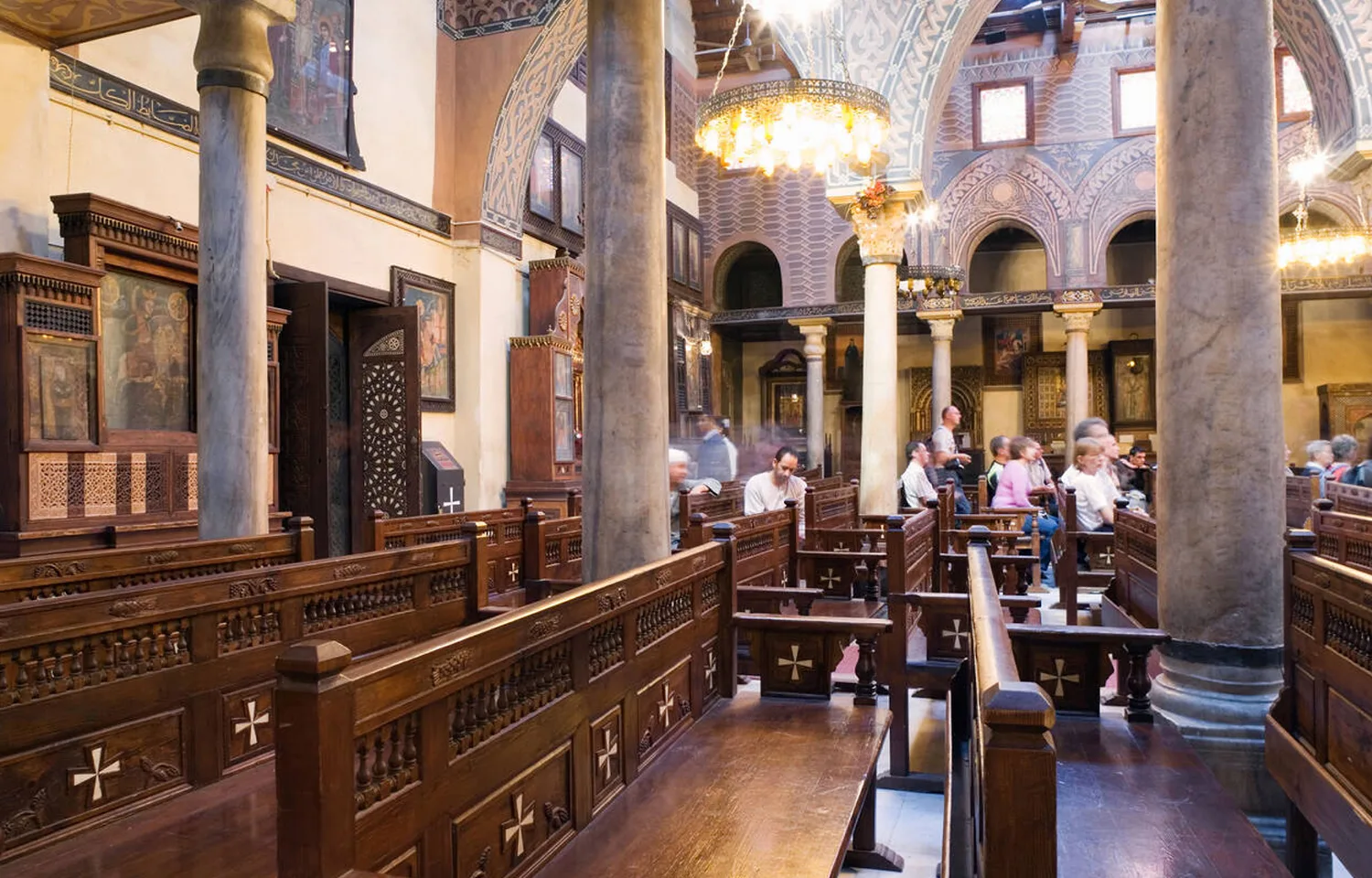 Interior of the Hanging Church in Coptic Cairo, showing wooden screens, marble columns, and seated visitors on a coptic cairo tour.