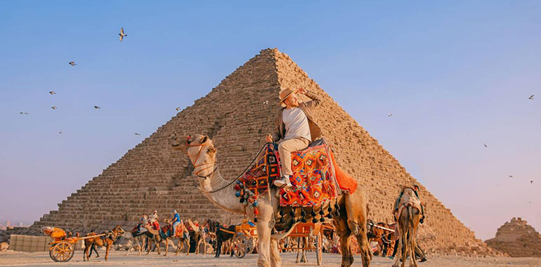 Happy Tourist man with hat riding on camel background pyramid of Egypt Giza