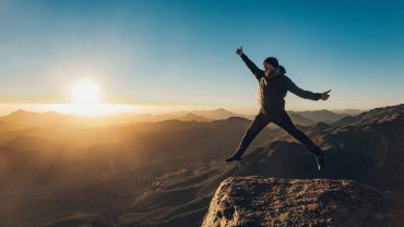 Man leaping with joy on a mountain peak at sunrise, overlooking the vast landscape of Mount Sinai.