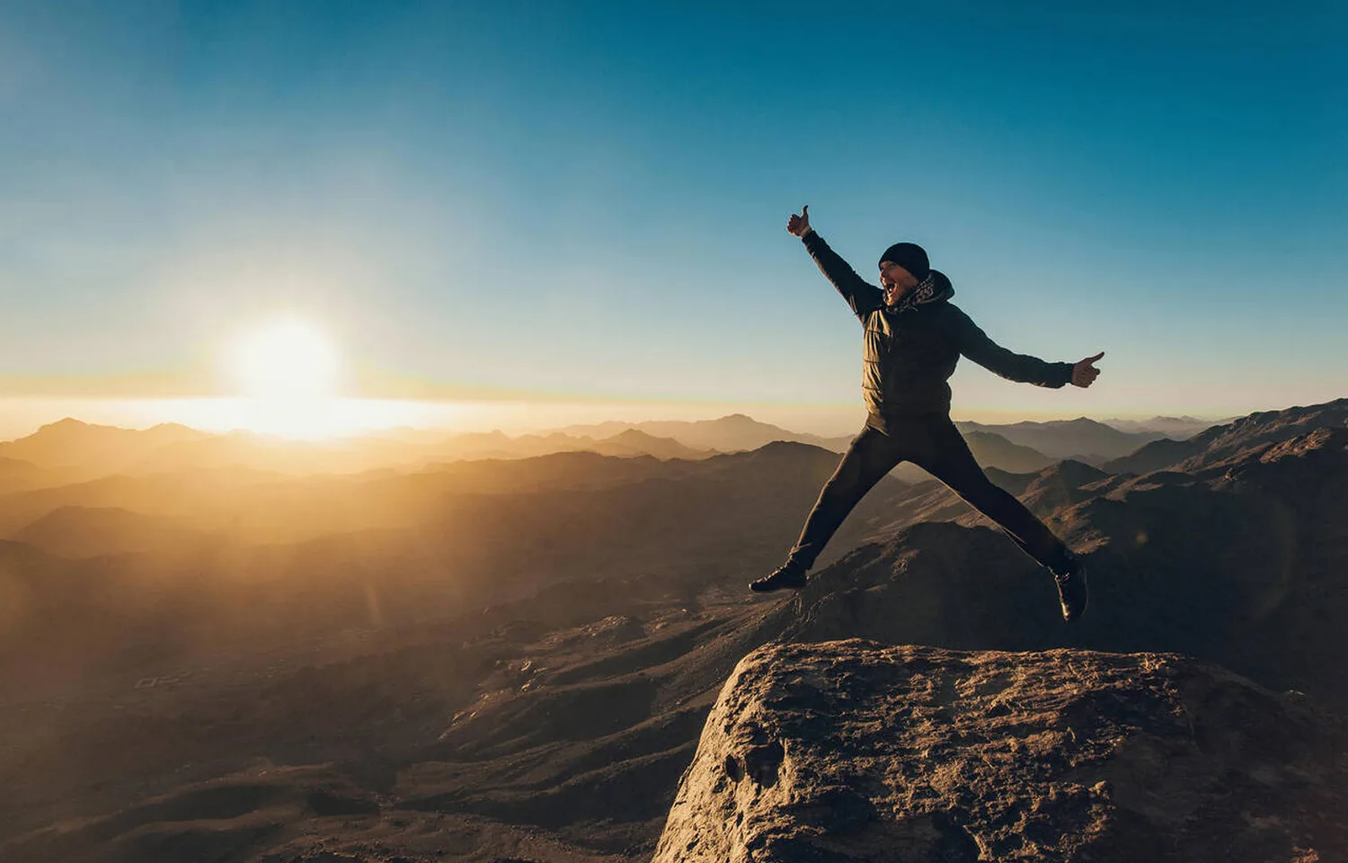 Man Leaping With Joy On A Mountain Peak At Sunrise, Overlooking The Vast Landscape Of Mount Sinai.
