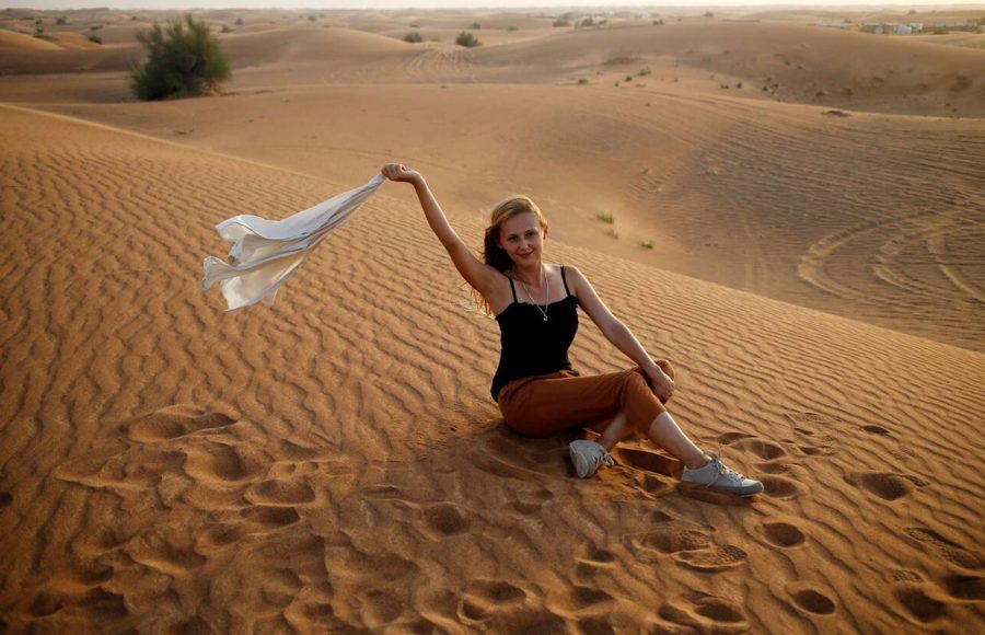 Happy-smiling-blonde-woman-sit-in-desert-sand-with-fluttering-on-wind-white-shirt-enjoy-safari-tour-in-Dubai