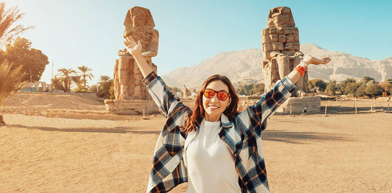 Happy Tourist Interested In Egyptology And Archaeology And Gets A Travel Experience At The Memnon Statue In