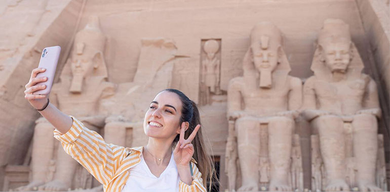 Happy Young Woman Tourist Taking A Selfie With The Famouse Abu Simbel Temple In The Back