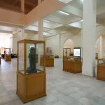 The large, modern, white-tiled exhibition hall of the Interior Of The Kharga Cultural Heritage Museum Of The Kharga Oasis, featuring artifacts displayed in wooden and glass cases.