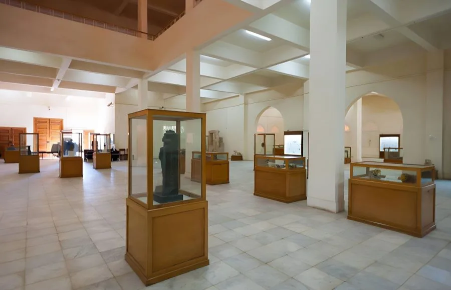 The large, modern, white-tiled exhibition hall of the Interior Of The Kharga Cultural Heritage Museum Of The Kharga Oasis, featuring artifacts displayed in wooden and glass cases.