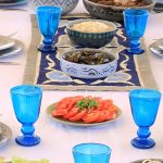 Close-up of a set dining table with blue glassware and Egyptian dishes.