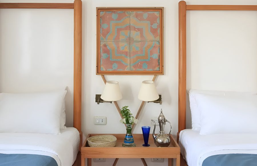 Close-up of two twin beds with white linens and a wooden nightstand featuring Egyptian decor.