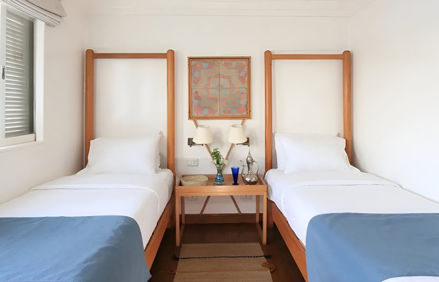 Wide shot of a twin cabin with blue bed runners and a central decorative nightstand.