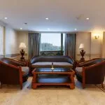 Oval-shaped outdoor swimming pool with submerged chairs facing a city skyline.