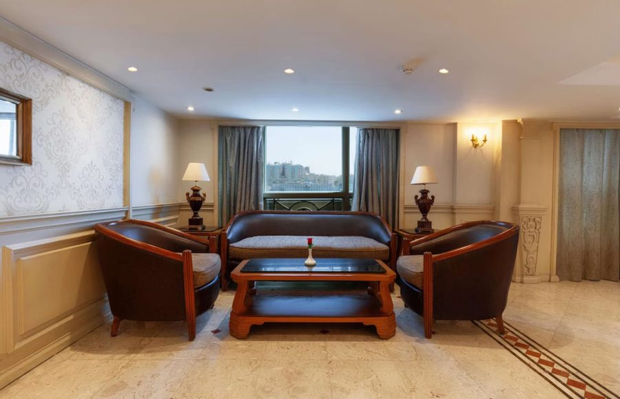 Oval-shaped outdoor swimming pool with submerged chairs facing a city skyline.