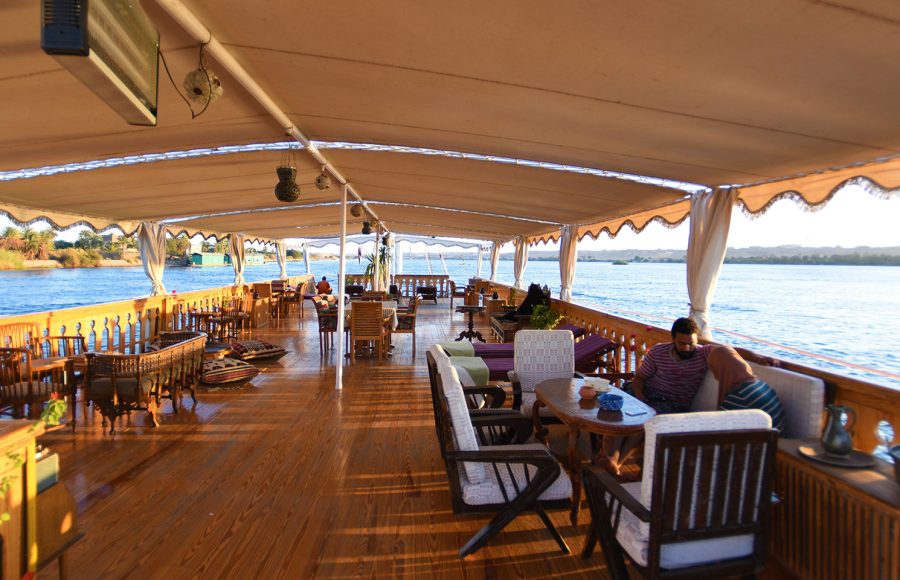 Expansive wooden sun deck of a Nile cruise ship with lounge seating and a canopy.